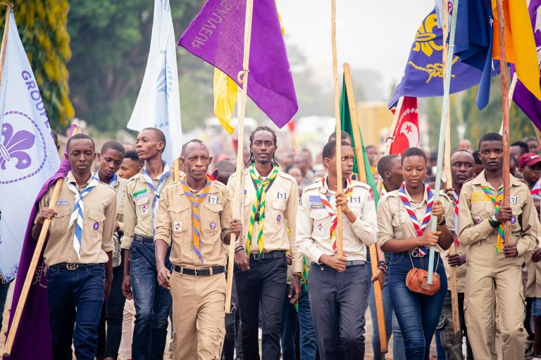A group of scouts proudly marching in a parade, showcasing colorful flags and uniforms.