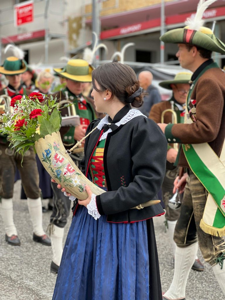 A vibrant procession featuring people in traditional Tyrolean attire carrying flowers in a lively street parade.