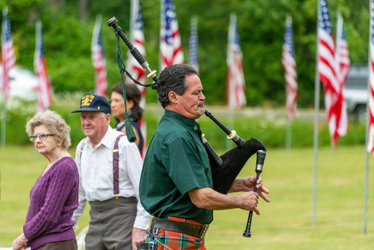 Bagpiper playing at an outdoor event with American flags, offering a vibrant cultural experience.